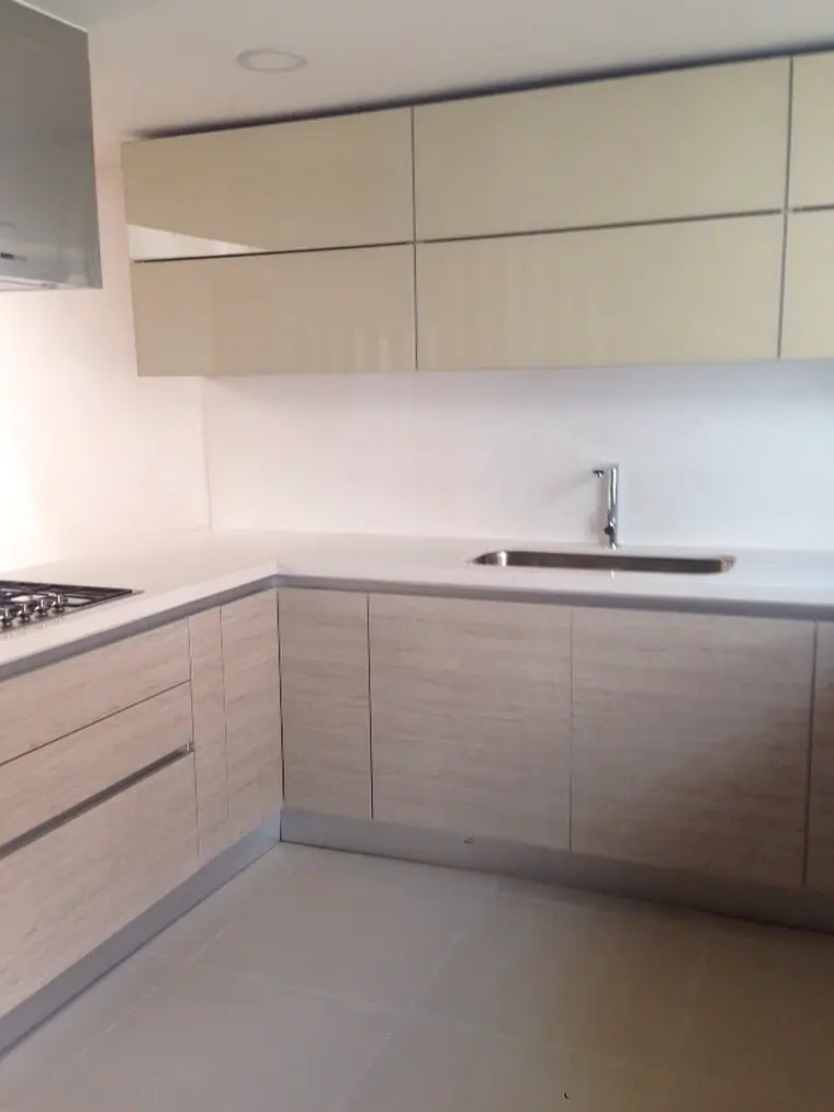 Cocina integral en L con muebles altos en alto brillo y base en enchape de madera clara