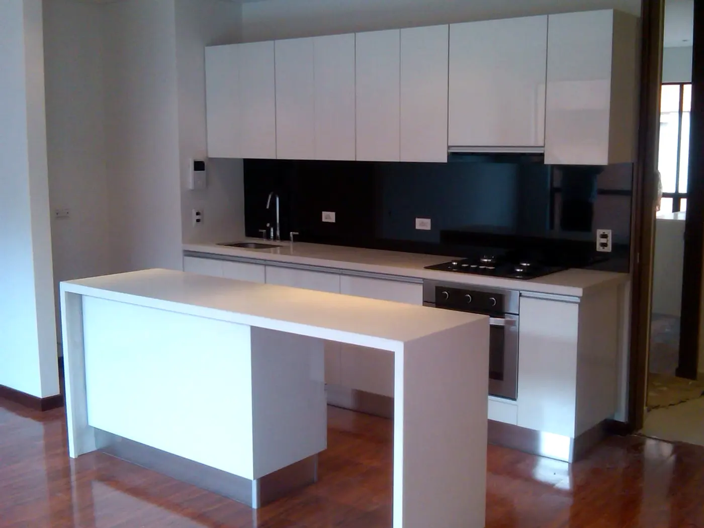 Cocina integral blanca en L con isla, barra auxiliar y salpicadero negro, fabricada por Decoración Raíz en Bogotá